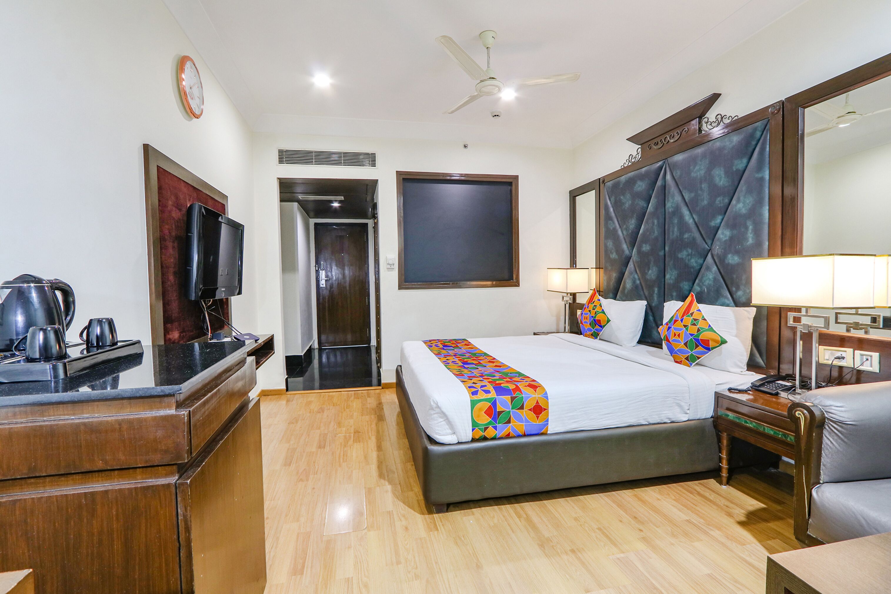 A hotel room with a bed, bedside table, lamp, and a television on a dresser.