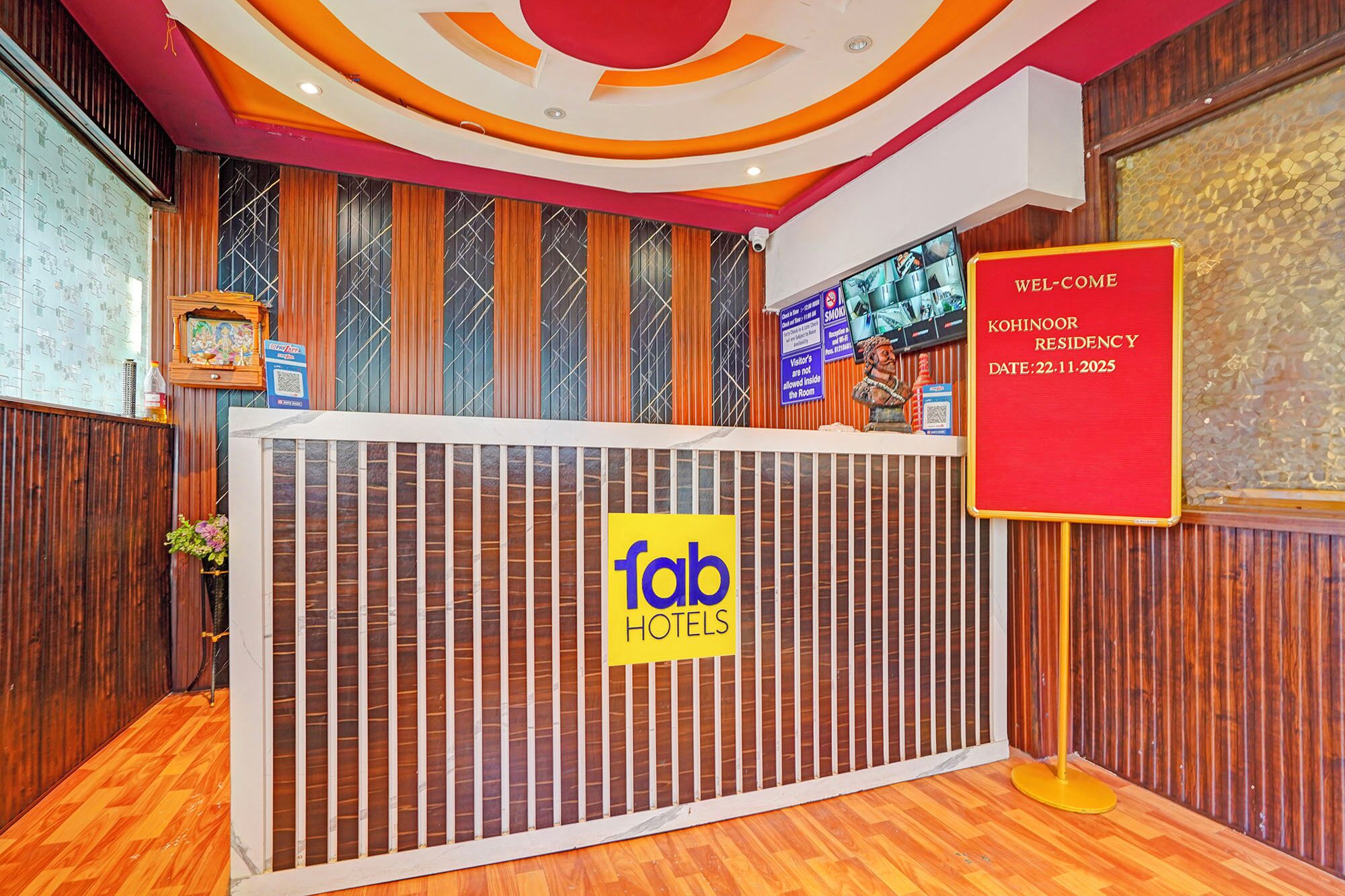 A reception desk with a 'fab hotels' sign, a 'wel-come kohinoor residency' sign, and a 'smoko' sign.