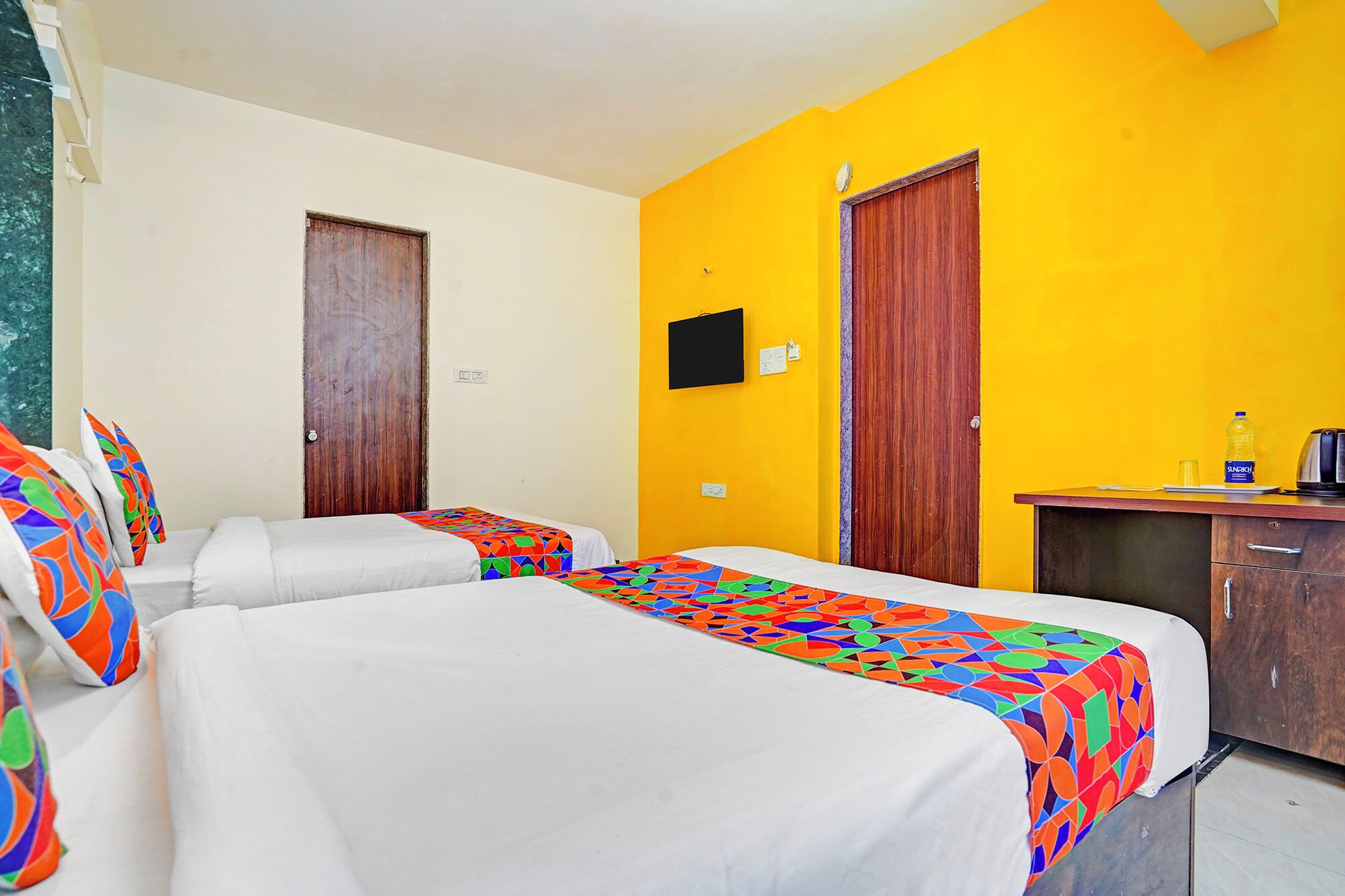 Une chambre d’hôtel avec deux lits, un bureau, une chaise et un téléviseur fixé au mur.