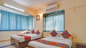 Two single beds with colorful geometric-patterned bedspreads, a wooden nightstand, a wall-mounted air conditioner, and a window with a blue patterned curtain. - FabHotel Kohinoor Residency I (Pune)