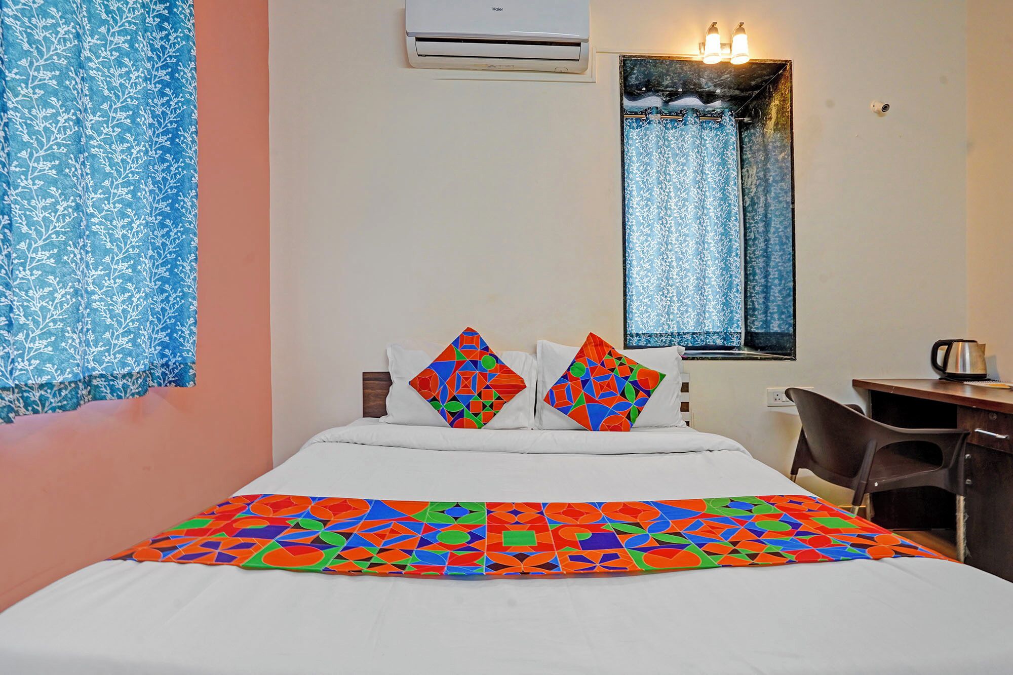 A hotel room with a bed, two pillows, a desk, a chair, and a window with curtains.