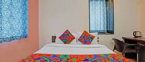 A hotel room with a bed, two pillows, a desk, a chair, and a window with curtains.