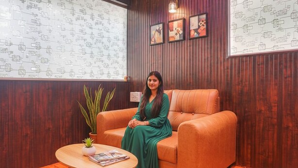 A woman sitting on an orange sofa in a room with wooden walls, a round wooden table with a plant, and framed pictures on the wall. - FabHotel Kohinoor Residency I (Pune)