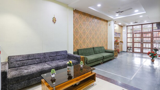 A spacious lobby with a grey and green sofa set, a wooden coffee table with plants, and a patterned wall. - Fabhotel Naresh Palace (Raipur)