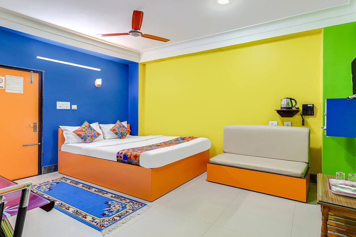 Una habitación con cama, sofá, ventilador de techo, televisor montado en la pared y una pequeña mesa con vasos y una tetera.