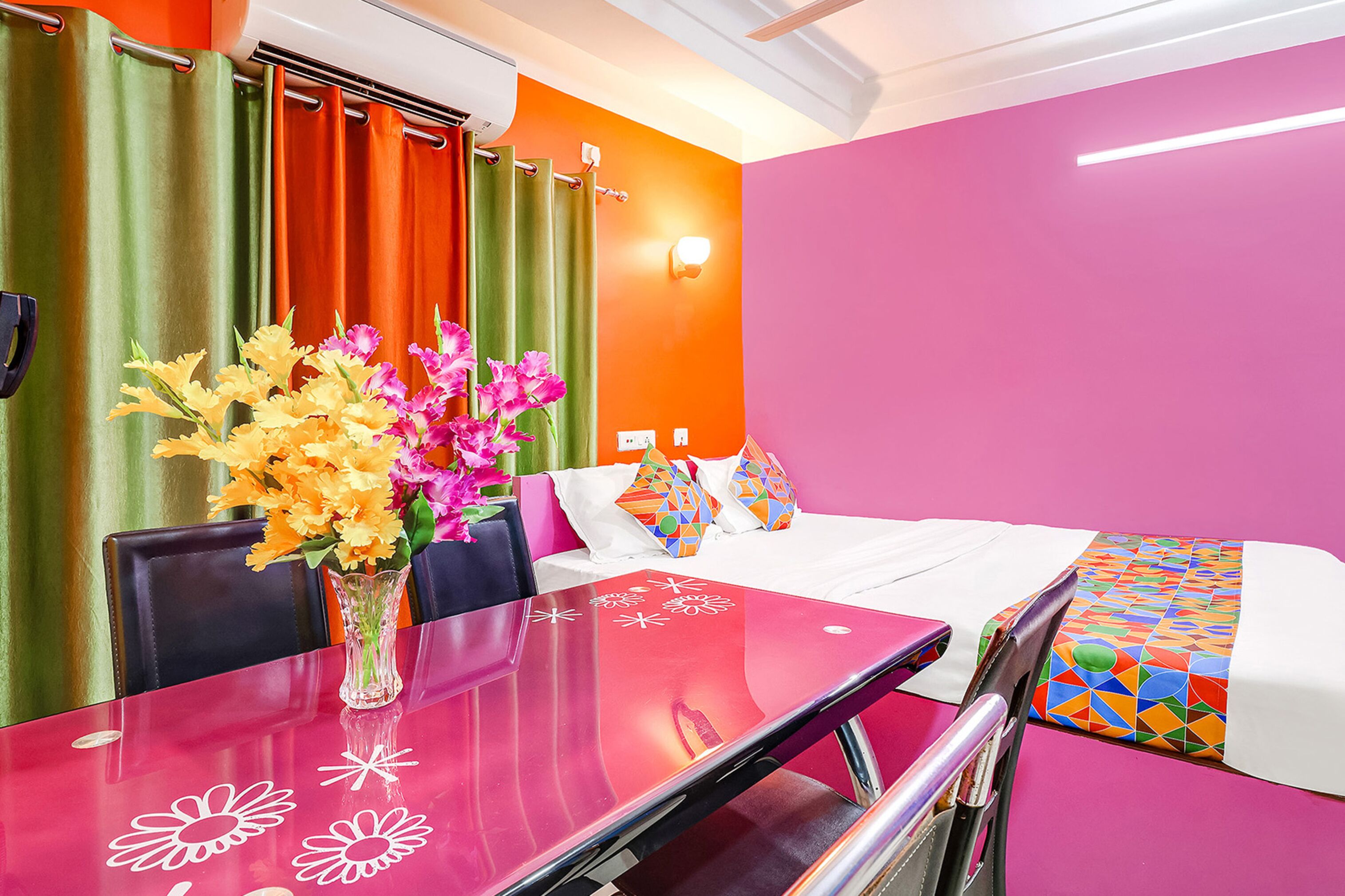 A hotel room with a bed, a table with a vase of flowers, and a bright orange wall.