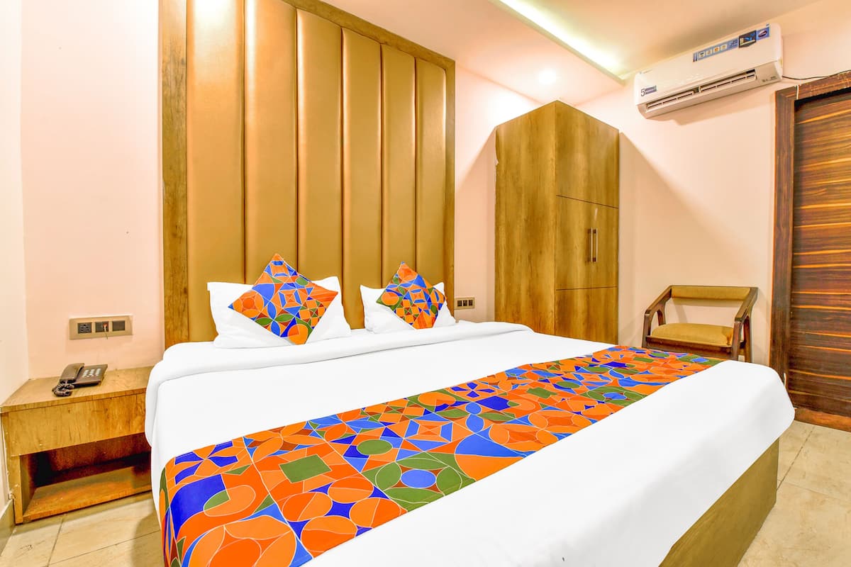 A hotel room with a bed, a nightstand, an air conditioning unit, a wooden wardrobe, and a chair.