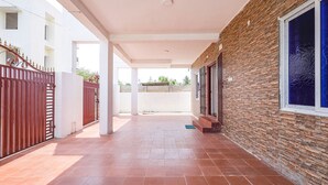 A covered corridor with tiled flooring, a brick wall on one side, and a white building on the other. - Fabexpress Kovalam Residency (Tirupporur)