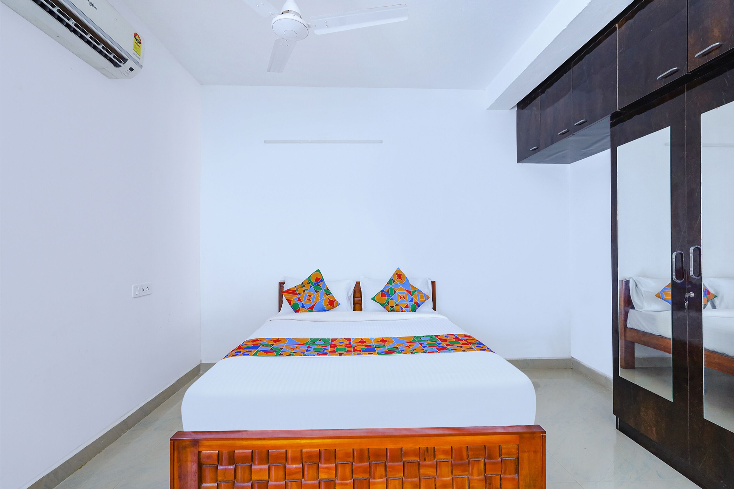 A bedroom with a bed, a ceiling fan, an air conditioner, and a wardrobe.