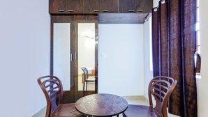 A small balcony with a round table and two chairs, a sliding glass door leading to a room with a bed, and a window with curtains. - Fabexpress Kovalam Residency (Tirupporur)