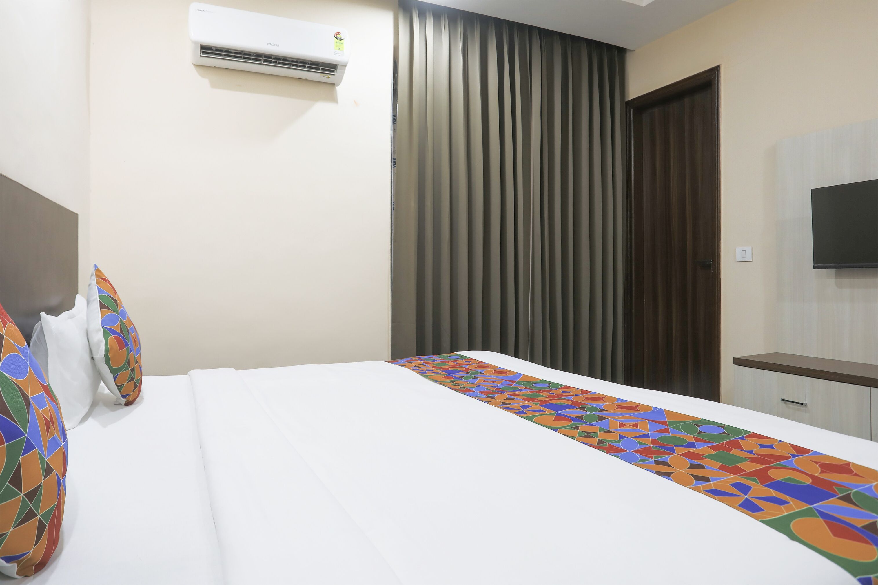A hotel room with a bed, a TV mounted on the wall, and a window with curtains.
