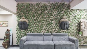 En grå modulsofa i et rum med en dekorativ væg med et gittermønster og to Buddha-statuer.