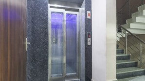 En elevator med kontrolpanel og en trappe med gelændere i metal.
