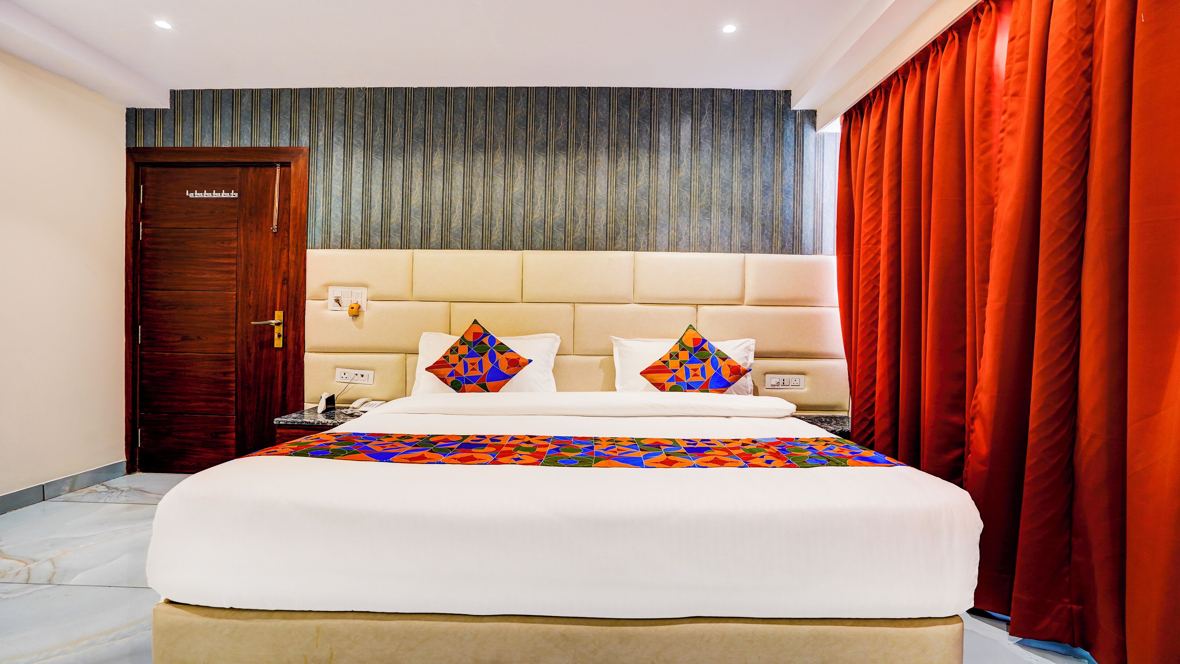 A hotel room with a large bed, a wooden door, a marble floor, and a red curtain.