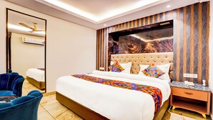 A hotel room with a large bed, a blue armchair, a nightstand, and a wall-mounted air conditioner. - FabHotel D2 - Nr Ashok Vihar (New Delhi)