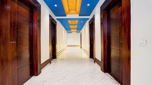 A hallway with wooden doors, a marble floor, and a blue ceiling with recessed lighting. - FabHotel D2 - Nr Ashok Vihar (New Delhi)