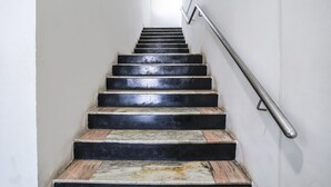 A staircase with alternating black and beige steps, a metal handrail, and white walls. - Fabexpress Raj Tourist (Nashik)