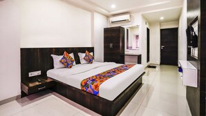 A modern hotel room with a large bed, a nightstand, a wardrobe, an air conditioning unit, and a ceiling fan. - Fabexpress Raj Tourist (Nashik)