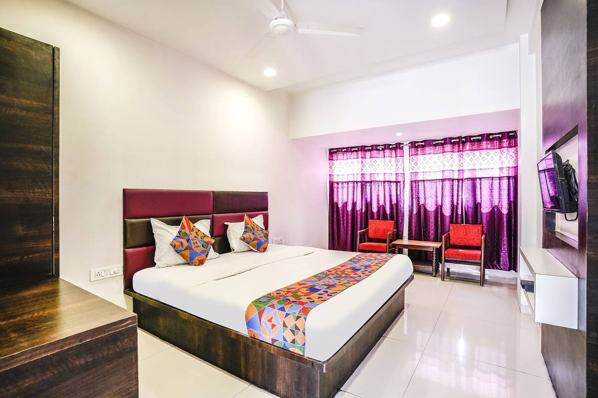 A modern hotel room with a large bed, a desk, a chair, and a TV.