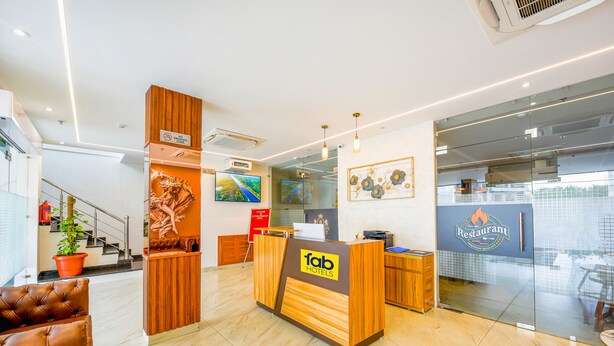 A hotel reception area with a wooden reception desk, a TV screen, and a glass wall reflecting the interior. - Fabhotel Prime Victoria Regency (Mohali)