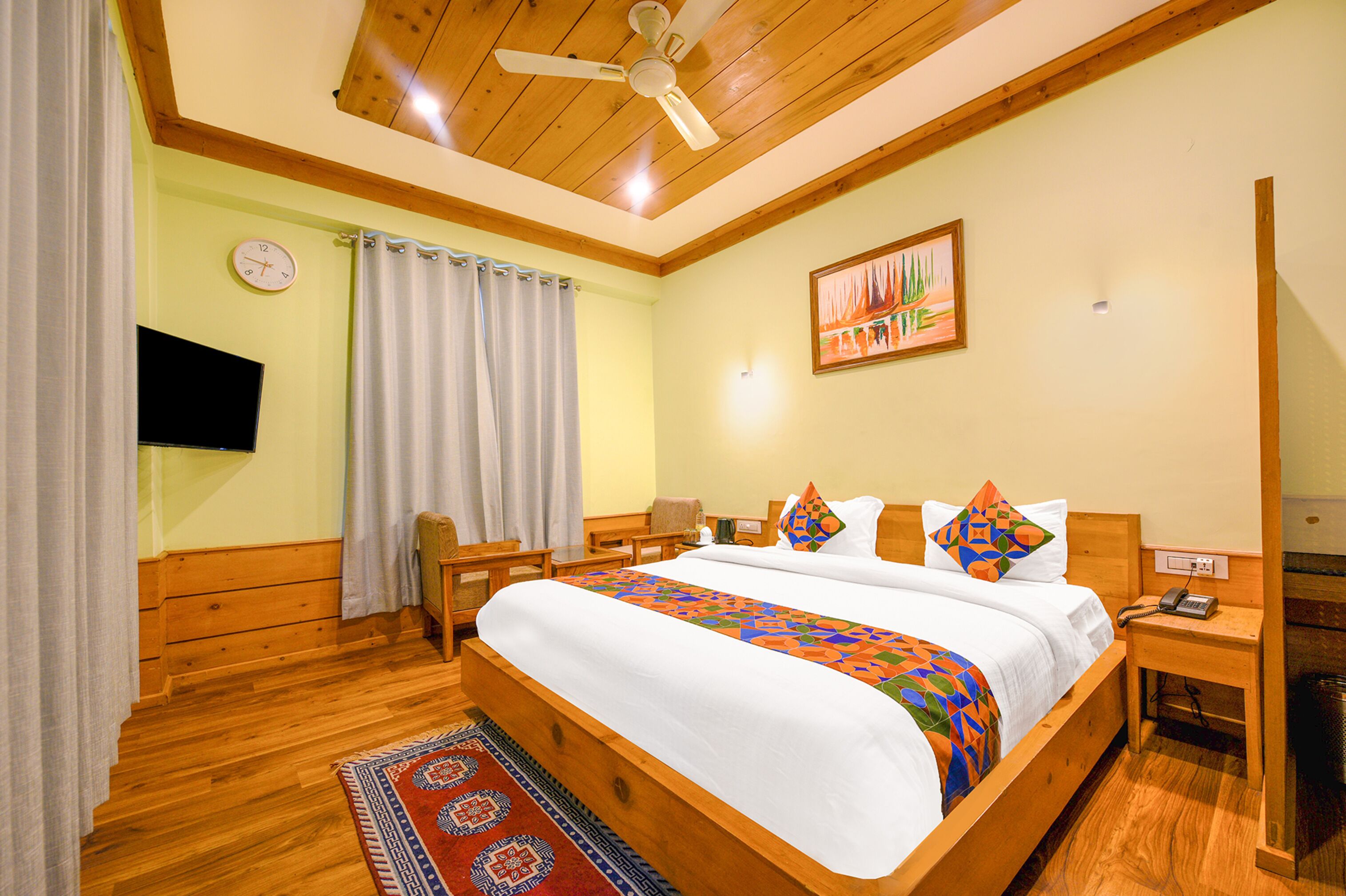 Habitación de hotel con cama de madera, ventilador de techo, reloj, pintura, escritorio y teléfono.