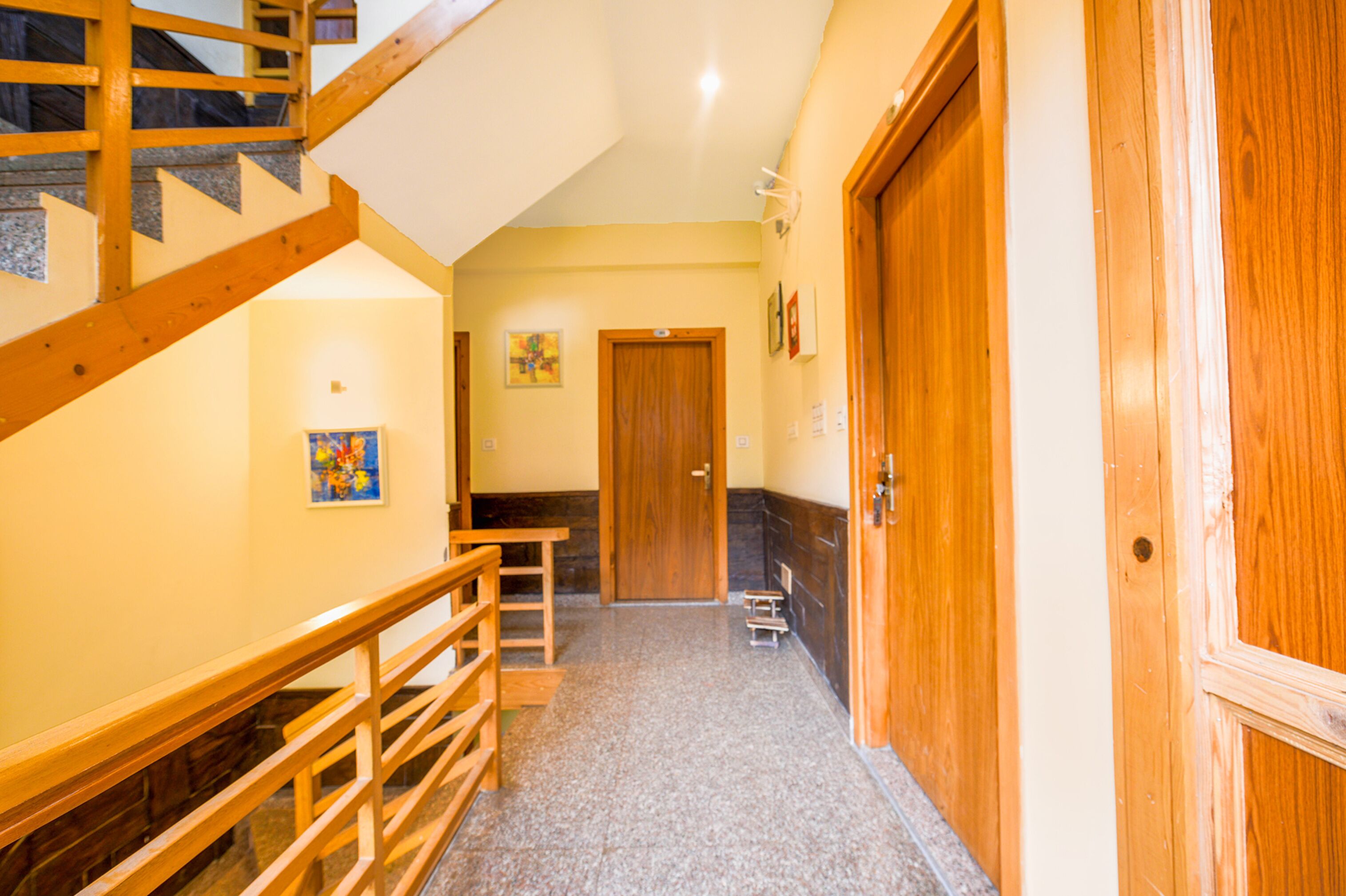 A hallway with wooden railings, a staircase, a door, and a small table.