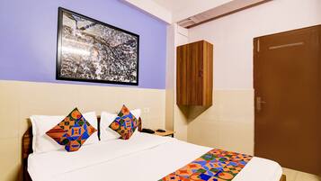 A hotel room with a bed, a framed picture on the wall, a wooden cabinet, and a door.