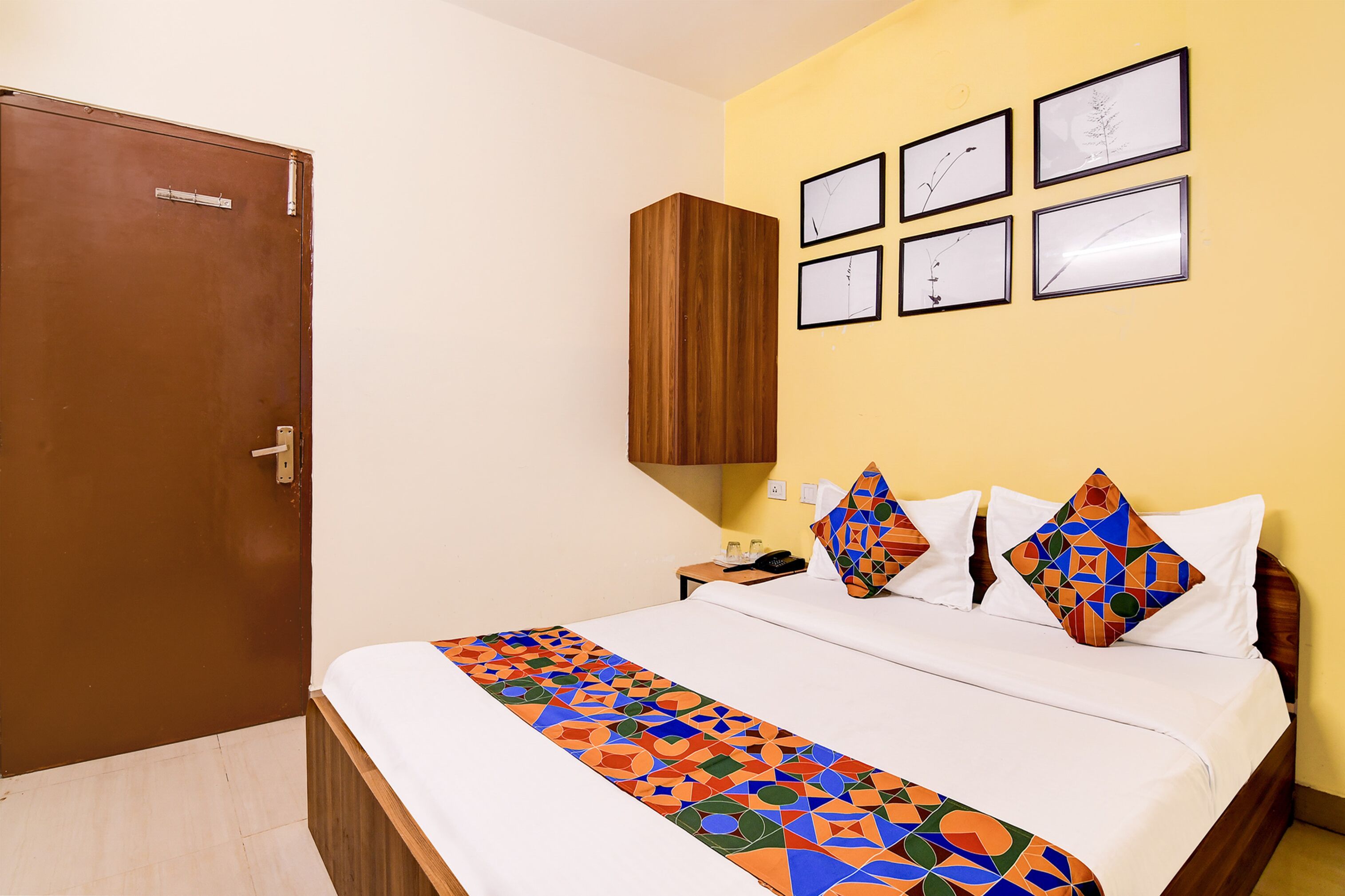 A hotel room with a bed, a wooden wardrobe, a nightstand, and a wall with framed pictures.