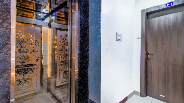 Entrada de hotel con puerta de madera marcada “101” y un ascensor de vidrio con paneles decorativos.