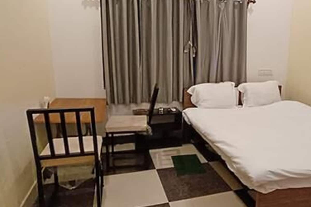Una habitación pequeña y limpia con cama, una silla, un escritorio y una ventana con cortinas.