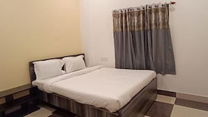 A bedroom with a bed, a nightstand, and a window with curtains. - Fabhotel Ocean Bird (Diamond Harbour)