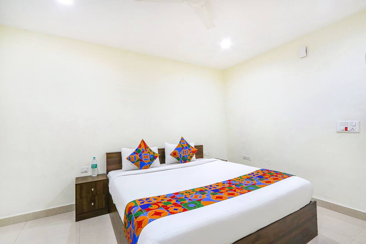 Une chambre d’hôtel avec un lit, une table de chevet, une bouteille d’eau et une prise électrique au mur.