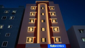 Ein mehrstöckiges Hotel mit auffälligem 'fabHOTELS'-Schild, das ein modernes Design mit beleuchteten Fenstern und einer zentralen, vertikalen Lichtleiste aufweist.