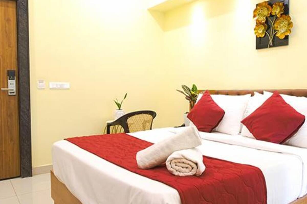 Una cama bien hecha con ropa de cama roja y blanca, un cabecero de madera y una pequeña planta en maceta sobre una mesita de noche.