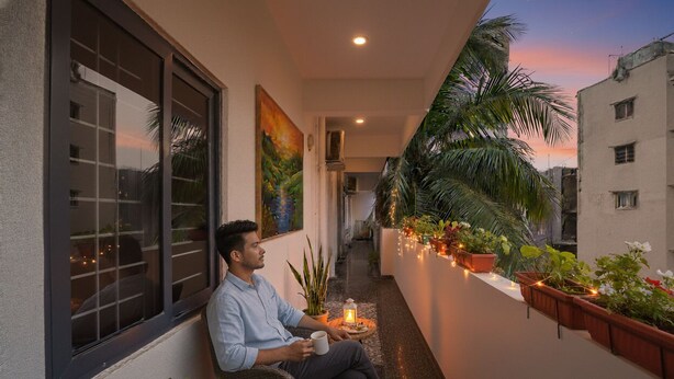 A man sitting on a balcony with a view of a sunset, holding a mug. - FabHotel Grand Aarvi Prime - Nr. Hafeezpet, Madeenaguda (Hyderabad)