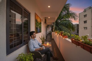 A man sitting on a balcony with a view of a sunset, holding a mug. - FabHotel Grand Aarvi Prime - Nr. Hafeezpet, Madeenaguda (Hyderabad)