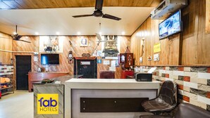 Un comptoir d’accueil avec une enseigne indiquant « fab hotels », un téléviseur fixé au mur et un ventilateur de plafond.