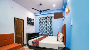 Une chambre à coucher avec un lit, un ventilateur de plafond, une fenêtre avec des rideaux à motifs floraux et une porte.