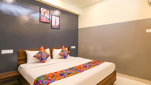 A neatly made bed with a colorful geometric-patterned bedspread, a white pillow, and a geometric-patterned pillow. The room has a dark gray wall with a framed picture and a light switch. - FabHotel Starhood - Manikonda (Hyderabad)