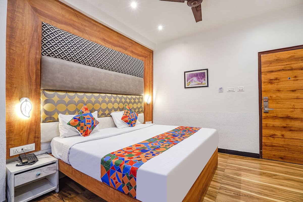 A hotel room with a wooden headboard, a bed with patterned pillows, a bedside table with a phone, and a door with a wooden frame.
