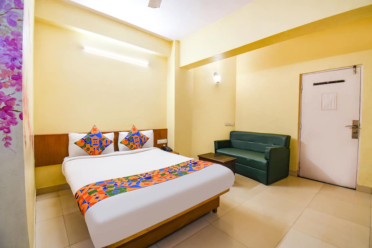 Quarto de hotel com uma cama, um sofá verde, uma porta e uma mesinha de cabeceira.