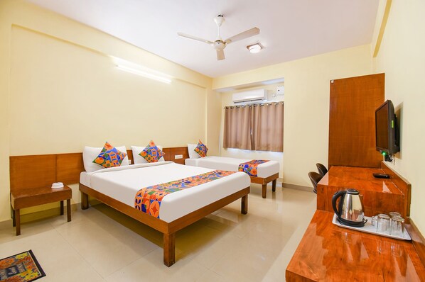 A hotel room with a large bed, two smaller beds, a desk with a kettle, a television, and a ceiling fan. - FabHotel Prime Yash Residency (Mawal)