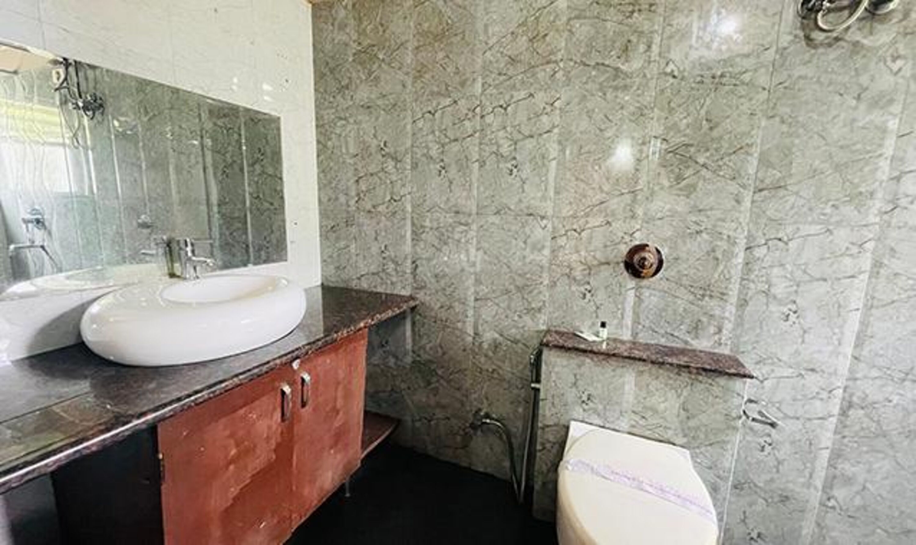 A bathroom with a marble wall, a sink, a mirror, and a toilet.