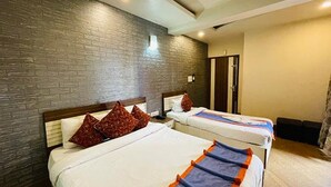 A hotel room with two beds, a brick wall, and a door. - Fabhotel Prime Gananayak (Jalpaiguri)
