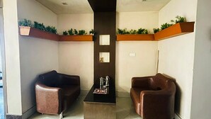 A lobby with two leather sofas, a black coffee table, and a dark wall with two framed pictures. - Fabhotel Prime Gananayak (Jalpaiguri)