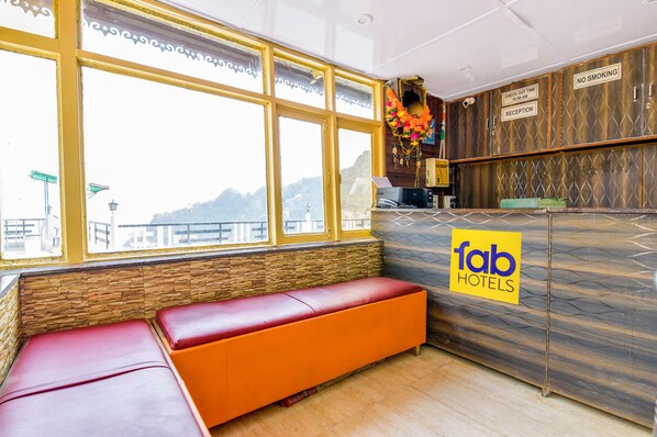 A reception area with a check-in counter, a reception desk, and a seating area with a bench. - FabExpress Sagar Plaza (Dehradun)