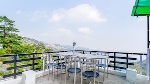 A terrace with tables and chairs, a lamp post, and a view of a hilly landscape. - FabExpress Sagar Plaza (Dehradun)