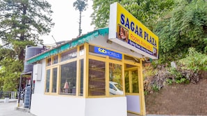 A small, single-story building with a yellow roof and large windows, labeled as 'Sagar Plaza' with a sign advertising rooms available. - FabExpress Sagar Plaza (Dehradun)
