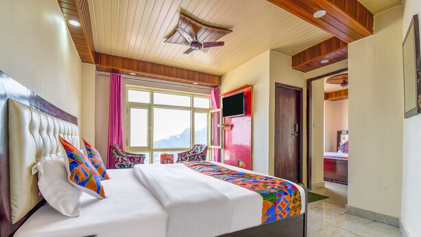 A hotel room with a bed, a ceiling fan, a TV, and a view of the mountains. - FabExpress Sagar Plaza (Dehradun)
