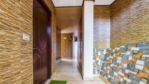 A hallway with stone-patterned walls, a wooden door, and a tiled section with a mosaic design. - FabExpress Sagar Plaza (Dehradun)